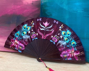 Può includere: Ventaglio decorativo con cornice in legno marrone scuro. Il ventaglio presenta un motivo floreale e di piume di pavone nei toni del rosa, del verde acqua e del viola. Un nappa rosa brillante pende dalla base del ventaglio.