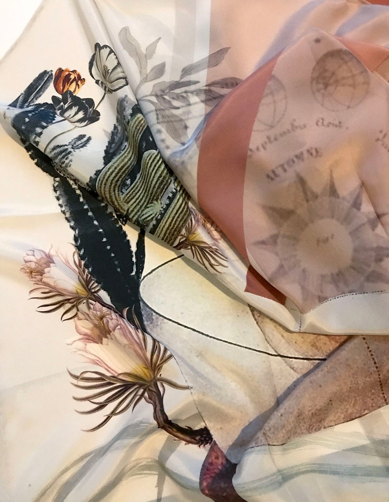 K&ouml;nnte beinhalten: Ein wei&szlig;er Seidenschal mit einem Blumendruck, der einen Kaktus, eine Blume und einen Zweig zeigt. Der Schal hat auf der R&uuml;ckseite ein pinkfarbenes und wei&szlig;es geometrisches Muster. Der Text "September, dont..." ist auf der R&uuml;ckseite des Schals sichtbar.
