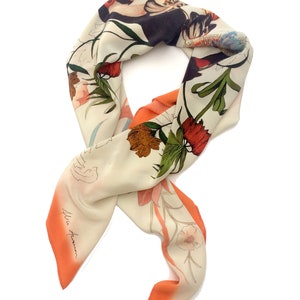 May include: A white silk scarf with a floral print in shades of orange, red, green, and black. The scarf has a gradient design with a peach color at the bottom. The scarf is signed "Ellie Forman" in the lower left corner.