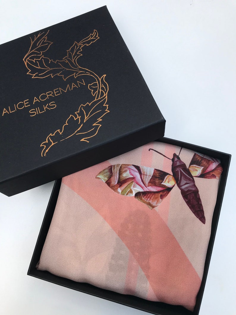 K&ouml;nnte beinhalten: Ein rosa Seidentuch mit einem braunen und gr&uuml;nen Schmetterlingsmuster. Das Tuch befindet sich in einer schwarzen Schachtel mit dem Text "Alice Acreman Silks" auf dem Deckel.