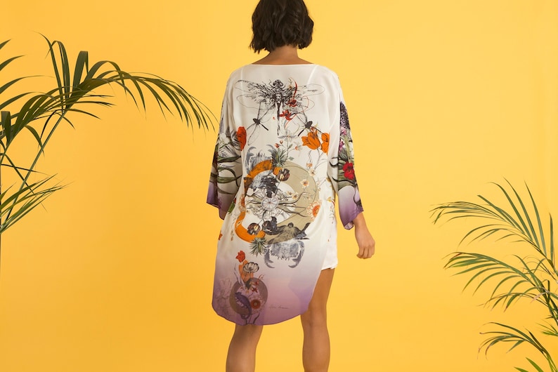 May include: A white kimono-style robe with a colorful floral and insect design. The robe has long sleeves and a purple ombre effect at the hem. The design includes orange, red, and green elements.