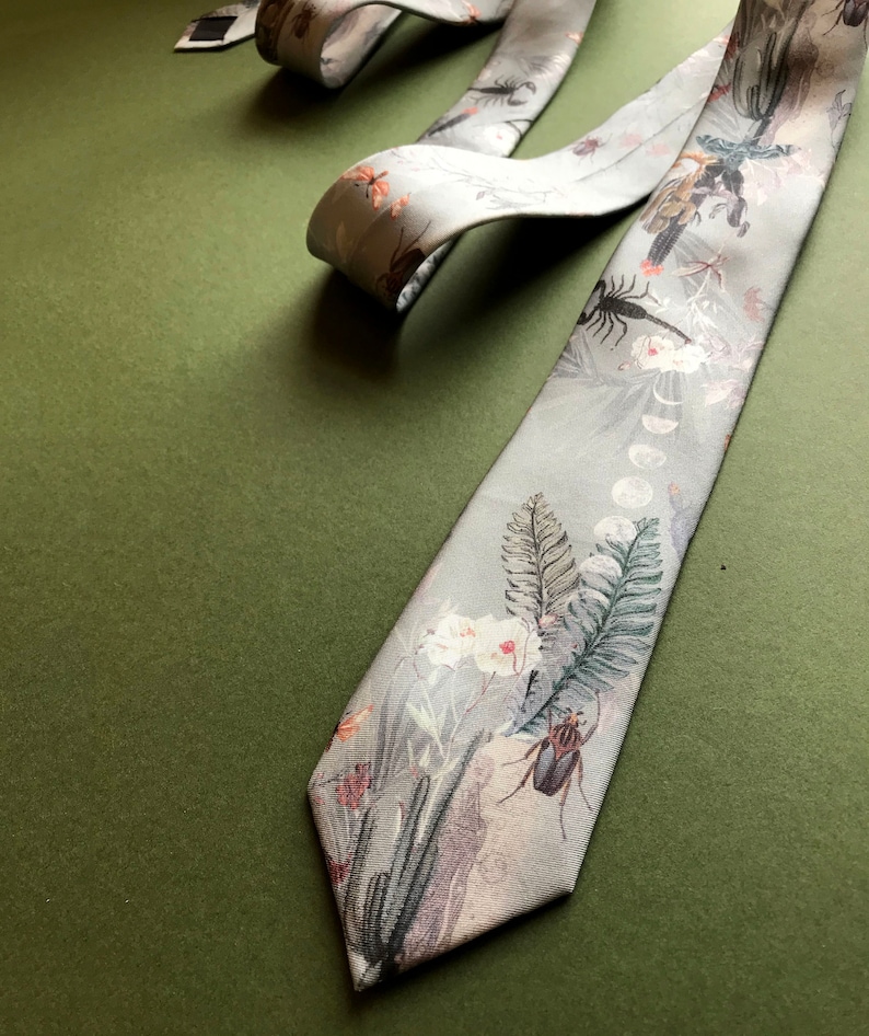 May include: A gray silk tie with a floral and insect print. The tie features a variety of insects, including beetles, scorpions, and dragonflies, as well as flowers and ferns. The tie is on a green background.