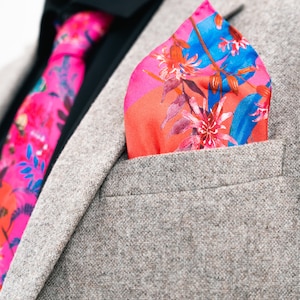 Può includere: Una giacca di abito in tweed marrone con un fazzoletto da taschino floreale e una cravatta floreale rosa. Il fazzoletto da taschino è piegato a punta e la cravatta è annodata con un nodo Windsor.