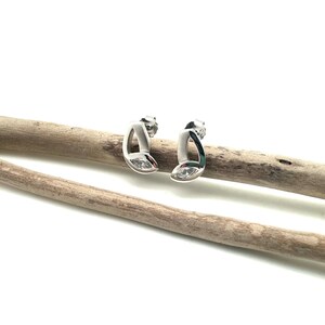 May include: A pair of silver earrings with a marquise-shaped clear stone set in each earring. The earrings are on a light brown wooden surface.