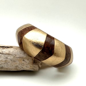 May include: A wide gold and brown bangle bracelet with a geometric pattern. The bracelet is made of wood and has a glossy finish.