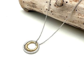 Könnte beinhalten: Eine silberne Kettenkette mit einem Doppelring-Anhänger. Der äußere Ring ist silber und der innere Ring ist gold.
