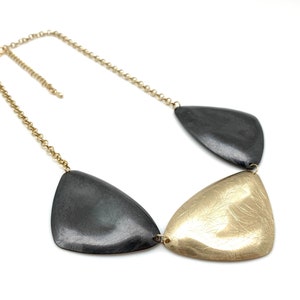 Puede incluir: Un collar de oro y negro con tres colgantes triangulares. Los colgantes están conectados por una cadena de oro.