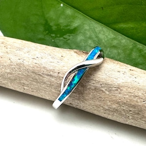 May include: A silver ring with a blue opal inlay in a twisted design. The ring is on a piece of driftwood.
