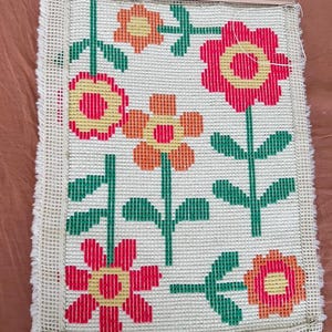 K&ouml;nnte beinhalten: Eine wei&szlig;e Leinwand mit einem bunten Blumenmuster. Die Blumen sind rot, orange und gelb mit gr&uuml;nen Stielen und Bl&auml;ttern. Die Leinwand ist mit einem Holzrahmen gerahmt.