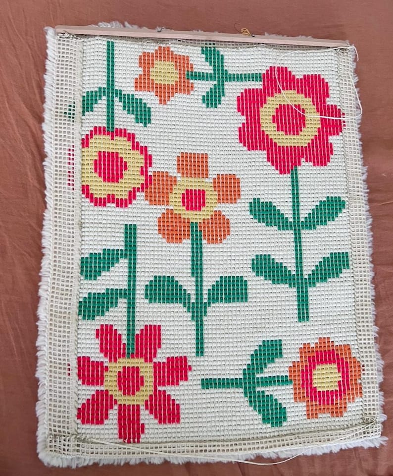K&ouml;nnte beinhalten: Eine wei&szlig;e Leinwand mit einem bunten Blumenmuster. Die Blumen sind rot, orange und gelb mit gr&uuml;nen Stielen und Bl&auml;ttern. Die Leinwand ist mit einem Holzrahmen gerahmt.