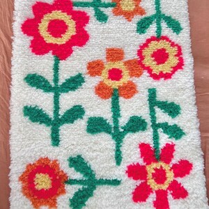 K&ouml;nnte beinhalten: Ein wei&szlig;er Teppich mit einem Blumendesign. Die Blumen sind rot, orange und gelb mit gr&uuml;nen Stielen und Bl&auml;ttern.
