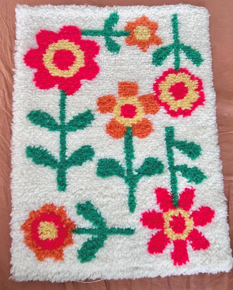 K&ouml;nnte beinhalten: Ein wei&szlig;er Teppich mit einem Blumendesign. Die Blumen sind rot, orange und gelb mit gr&uuml;nen Stielen und Bl&auml;ttern.