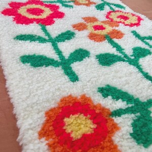K&ouml;nnte beinhalten: Ein wei&szlig;er Teppich mit einem Blumendesign. Die Blumen sind orange, rot und gelb. Der Teppich ist aus einem flauschigen Material.