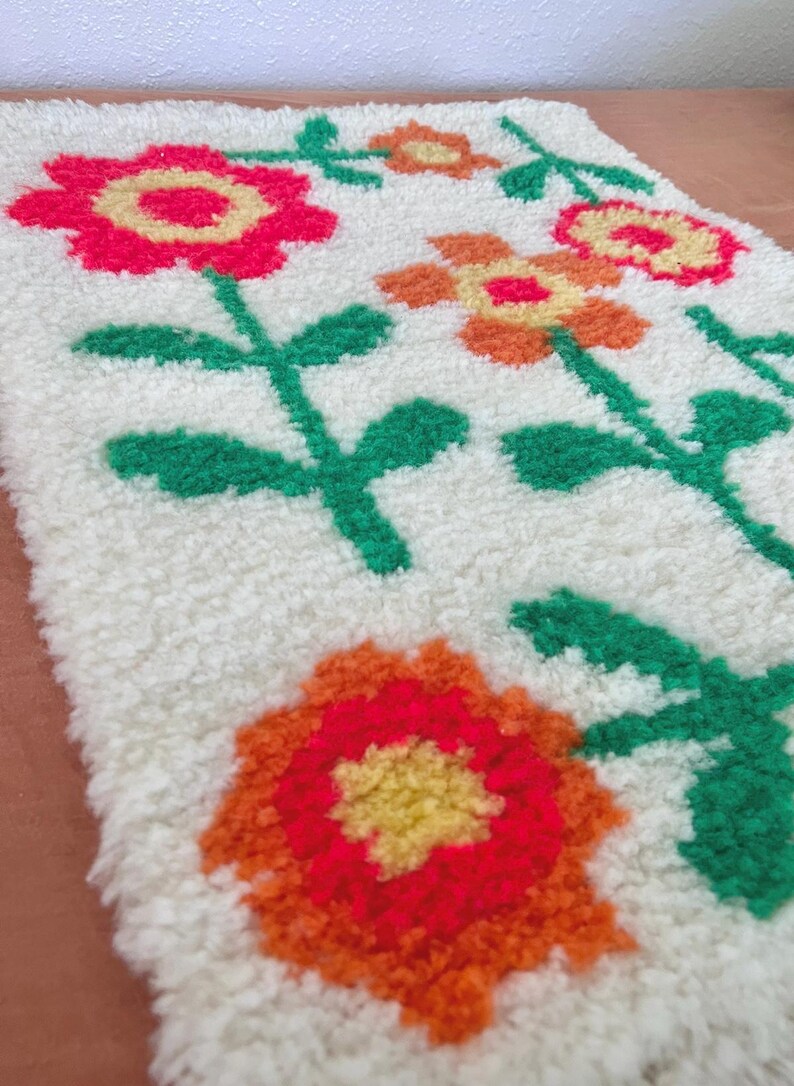 K&ouml;nnte beinhalten: Ein wei&szlig;er Teppich mit einem Blumendesign. Die Blumen sind orange, rot und gelb. Der Teppich ist aus einem flauschigen Material.