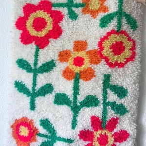 K&ouml;nnte beinhalten: Ein wei&szlig;er Teppich mit einem Blumendesign. Die Blumen sind rot, orange und gelb mit gr&uuml;nen Stielen und Bl&auml;ttern.