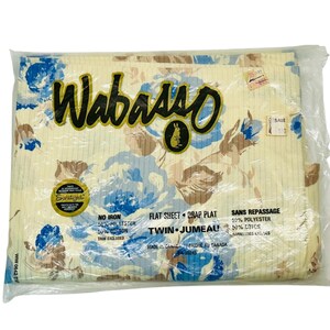 May include: A white twin-sized flat sheet with a floral print in shades of blue, brown, and beige. The sheet is packaged in plastic and has a label that reads "Wabasso" and "Twin Jumeau".