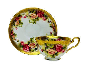 May include: A white teacup and saucer set with a gold rim and handle. The cup and saucer are decorated with red and pink roses and green leaves. The set is likely made of porcelain.