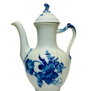 May include: White porcelain coffee pot with a lid and a curved spout. The pot is decorated with blue floral designs and accents. The handle and the top of the lid are also painted blue. The pot has a textured surface.