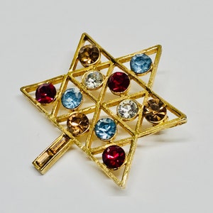May include: A gold-toned Star of David brooch with a geometric design and colourful rhinestones. The rhinestones are in shades of red, blue, and brown.
