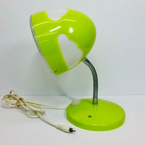 May include: A green and white desk lamp with a flexible arm and a round base. The lampshade has a unique design with white shapes on a green background.