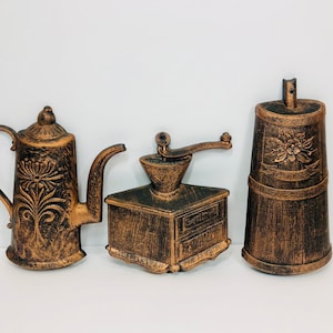 Puede incluir: Tres piezas de decoración de pared de metal de estilo antiguo en un acabado marrón rústico. Las piezas son una cafetera, un molinillo de café y una lata de café. Cada pieza tiene un diseño floral.
