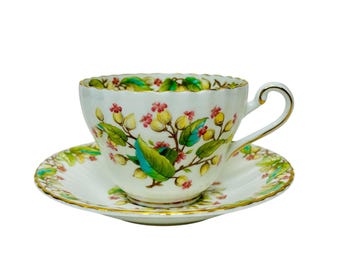 Peut inclure: Une tasse à thé et une soucoupe blanches avec un motif floral dans des tons de vert, jaune et rose. Le motif floral présente de petites fleurs et des feuilles.