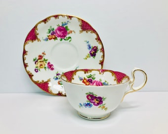 May include: A vintage teacup and saucer set with a pink and gold floral pattern. The cup and saucer have a scalloped edge and are decorated with a delicate floral design in shades of pink, yellow, and blue.
