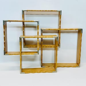 May include: A set of four wooden wall shelves with silver metal accents. The shelves are arranged in a geometric pattern and are perfect for displaying small items.