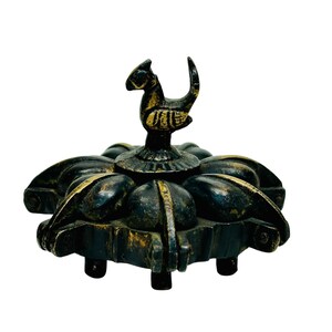 May include: An antique-style metal ornament featuring a bird figure. The base is dark with gold detailing, and the bird is adorned with gold and black. The object has an intricate design, possibly a decorative item or a small sculpture.