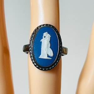 May include: Oval-shaped ring with a blue cameo design. The ring features a silver-colored band and a blue oval center with a white relief figure. The ring is a classic piece of jewelry.