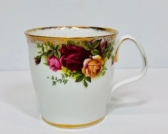 May include: White teacup with a gold rim and a floral design featuring red, pink, and yellow roses.