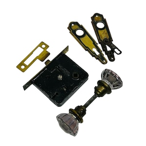 May include: Antique brass door hardware set with a black metal lock, two brass plates, and two glass door knobs with a purple tint.