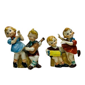 Peut inclure: Un ensemble de quatre figurines en porcelaine vintage représentant des enfants jouant de la musique. Les figurines sont peintes dans des couleurs vives et présentent une fille jouant de la guitare, un garçon jouant de l'accordéon, une fille dansant et un garçon jouant du tambour.