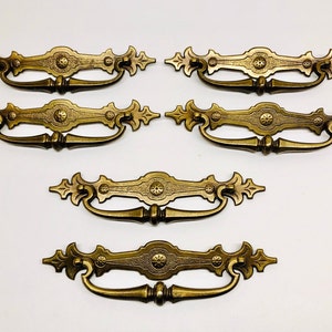 May include: Set of six ornate gold-toned cabinet drawer pulls with a decorative floral design. Each pull has a center rosette and a curved handle.