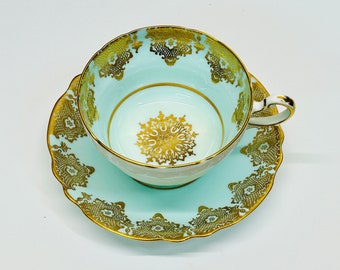 May include: A light blue teacup and saucer set with gold trim and intricate floral designs. The cup and saucer are decorated with a delicate lace pattern.