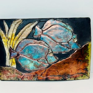 May include: A ceramic wall art piece depicting two blue and green fish with iridescent accents, set against a black background with yellow and orange accents.