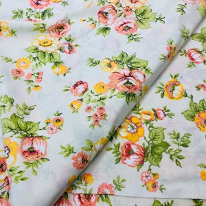 Puede incluir: Tela blanca con estampado floral con flores rosas y amarillas. La tela est&aacute; doblada por la mitad, mostrando el patr&oacute;n en ambos lados.