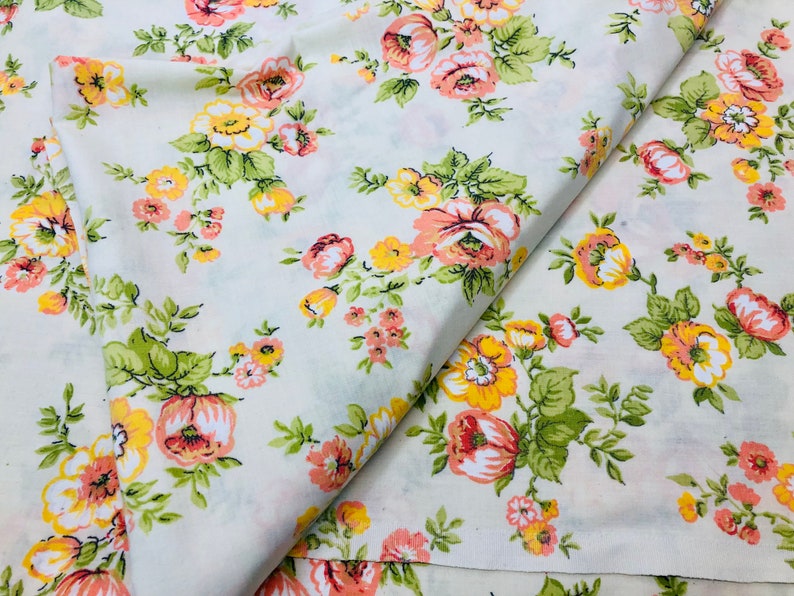 Puede incluir: Tela blanca con estampado floral con flores rosas y amarillas. La tela est&aacute; doblada por la mitad, mostrando el patr&oacute;n en ambos lados.