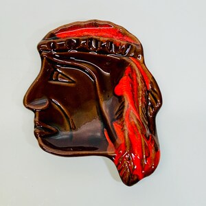 May include: A brown ceramic ashtray shaped like a Native American man's head with red and orange feathers.