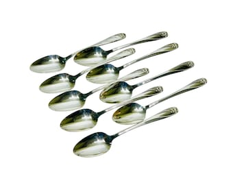 May include: A collection of nine shiny, silver spoons arranged diagonally against a white background. Each spoon has a rounded bowl and a decorative handle. The spoons are clean and reflect light.