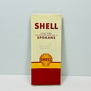 May include: A vintage Shell street guide and metropolitan map of Spokane, Washington. The guide is printed on cream paper with red and yellow accents. The Shell logo is a yellow seashell on a red background.