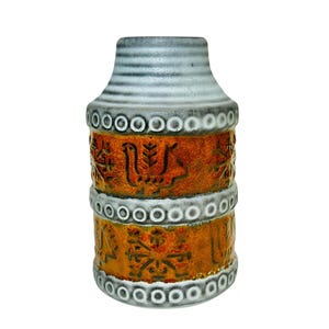 May include: A ceramic vase with a cylindrical shape, featuring a textured surface. The vase has a white and gray striped top, with orange and brown bands adorned with embossed patterns and a ring of white dots.