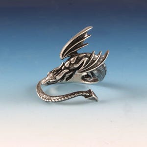 May include: A silver dragon ring with a detailed design. The dragon's wings are spread out and its tail is curled around the ring.