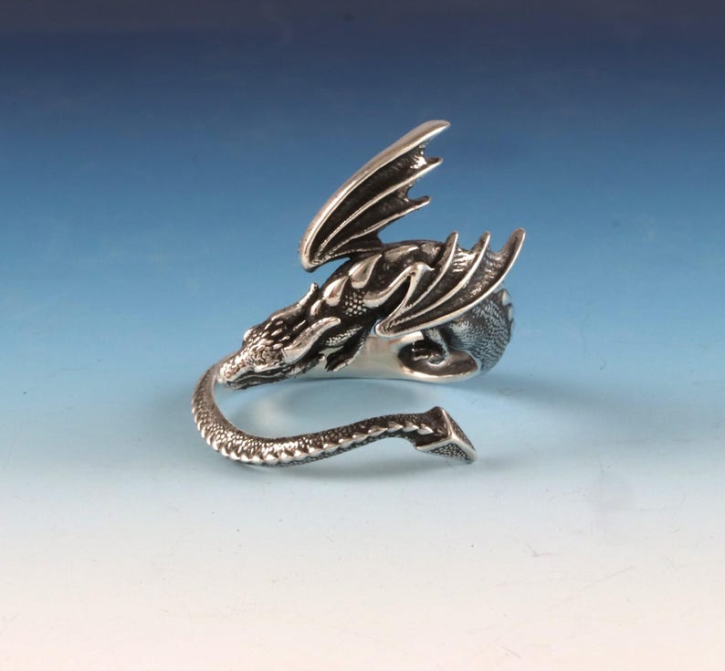 May include: A silver dragon ring with a detailed design. The dragon's wings are spread out and its tail is curled around the ring.