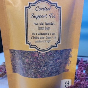 May include: A brown paper bag of Cortisol Support Tea. The label includes the tea's name and ingredients: rose, tulsi, lavender, and lemon balm. Instructions suggest steeping the tea for 5-10 minutes. The bag is partially transparent, revealing the tea blend.