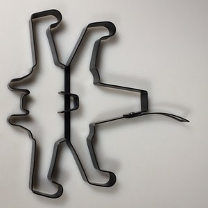 May include: A black metal silhouette of a person with outstretched arms and legs. The silhouette is made of a single piece of metal and is bent into a unique shape.