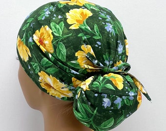 Peut inclure: Un bonnet de chirurgien à motifs floraux avec un fond vert foncé, des fleurs jaunes, des feuilles vertes et de petites fleurs bleues. Le bonnet est noué en chignon à l'arrière.