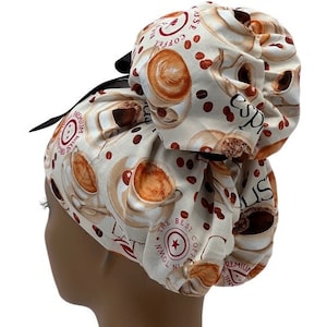 May include: A white scrub hat with a coffee cup and bean print. The hat has a black ribbon and the text "The Best Coffee In Town" is printed on the hat.