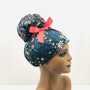 May include: A dark blue scrub hat with a floral print and a red bow. The hat is designed to be worn with a ponytail.