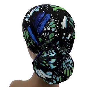 May include: A black head covering with a butterfly wing pattern in shades of blue, green, and white. The head covering is tied in a bun at the back. The fabric has a soft, flowing appearance.